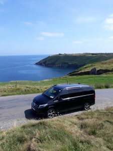 black mercedes benz v class v250d on the background of blue sea and green cliffs